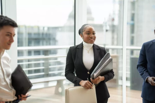 Trainee solicitor at a London law firm holding documents during a meeting in a modern office with city views.