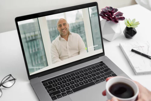 Video of a law firm partner displayed on a laptop screen, with a person holding a coffee cup at a desk.